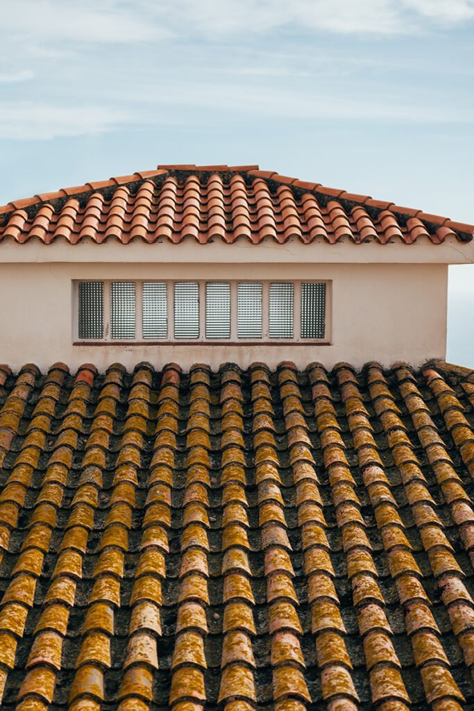 Roof of a house with small window and terracotta tiles.